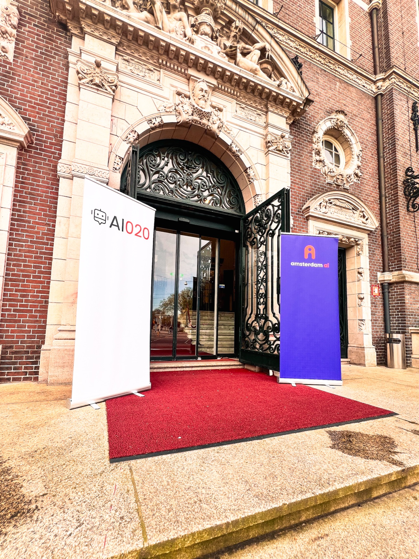 The AI020 venue entrance in Amsterdam — ornate brick building with AI020 banners flanking the doors.