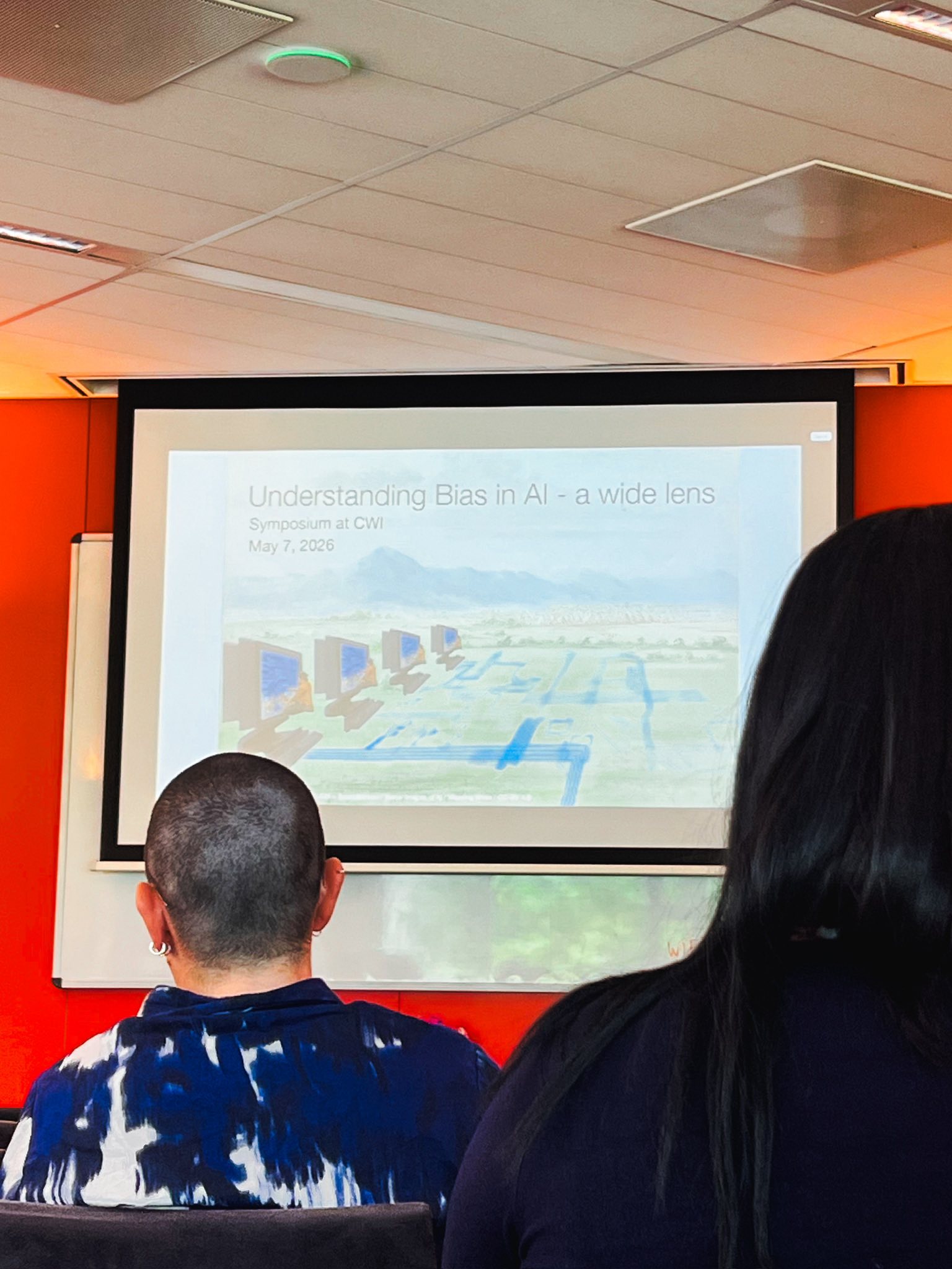 A projection screen reading 'Understanding Bias in AI — a wide lens, Symposium at CWI, May 7, 2026'.