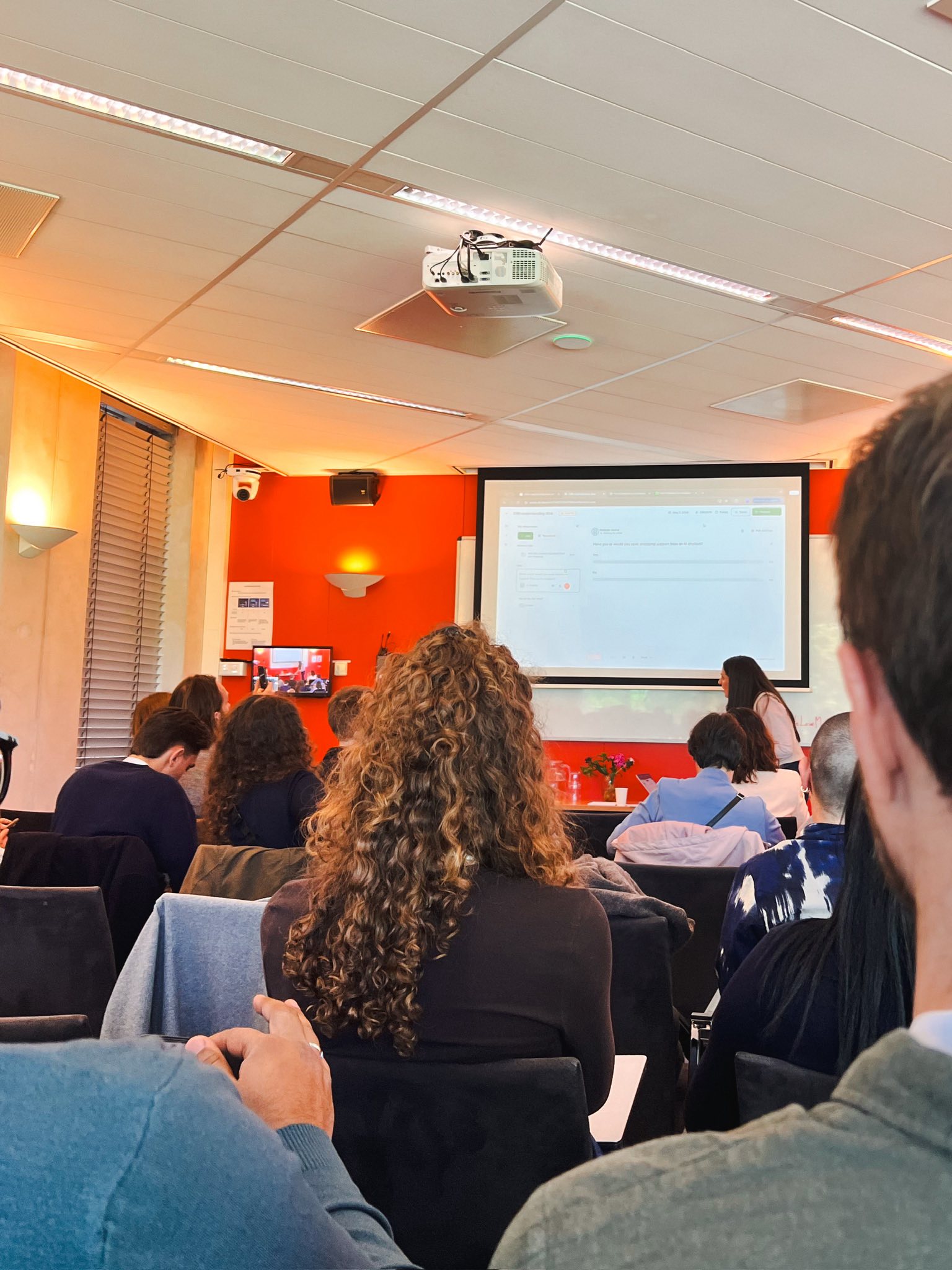 A packed room of researchers facing a screen showing an interface mockup during a talk.